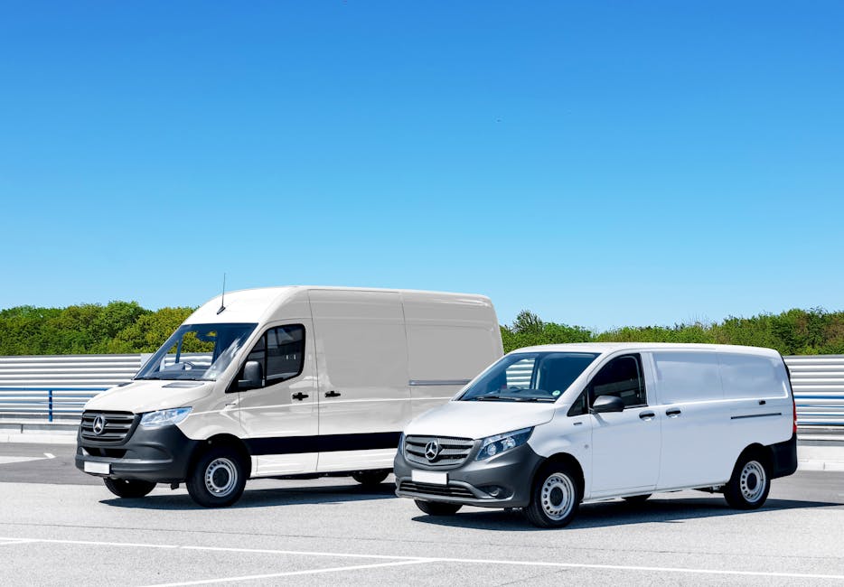 Two white Mercedes-Benz panel vans parked side by side on a brightly lit outdoor road, with a metal guardrail and green trees in the background under a clear blue sky. The larger van on the left has a high roof and is positioned slightly behind the smaller van on the right. Both vehicles are used for home relocation, with their sliding side doors closed. The scene suggests a moving or furniture transport process, with the vans ready for loading or unloading. The environment appears clean and spacious, suitable for loading household furniture, boxes, and packing materials such as cardboard boxes, wrapping, and blankets, which are implied to be inside or being prepared for transport. Man With a Van Hillingdon offers professional removals, and these vehicles are typical for assisting with packing and moving tasks, including furniture transport and loading process, along a designated route or property driveway.