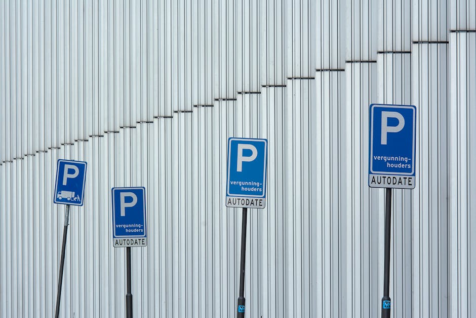 Four blue parking permit signs mounted on black metal poles are positioned along a paved area adjacent to a large silver corrugated metal wall, with the signs indicating parking permissions for moving vans or trucks. The signs display a white 'P' symbol, accompanied by text in Dutch, including words like 'vergunninghouders' and 'AUTODATE,' suggesting permitted parking for authorized vehicles related to house removals or moving services. The environment appears to be an outdoor area designated for vehicle parking during home relocation, with the signs supporting the process of furniture transport and loading logistics managed by companies such as Man With a Van Hillingdon. The lighting is natural, and the overall scene emphasizes parking regulations relevant to moving day activities, directly connecting to the topic of Hillingdon Council parking permits for moving vans.