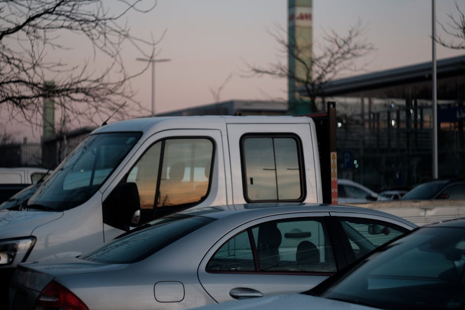 Two white Mercedes-Benz panel vans parked side by side on a brightly lit outdoor road, with a metal guardrail and green trees in the background under a clear blue sky. The larger van on the left has a high roof and is positioned slightly behind the smaller van on the right. Both vehicles are used for home relocation, with their sliding side doors closed. The scene suggests a moving or furniture transport process, with the vans ready for loading or unloading. The environment appears clean and spacious, suitable for loading household furniture, boxes, and packing materials such as cardboard boxes, wrapping, and blankets, which are implied to be inside or being prepared for transport. Man With a Van Hillingdon offers professional removals, and these vehicles are typical for assisting with packing and moving tasks, including furniture transport and loading process, along a designated route or property driveway.